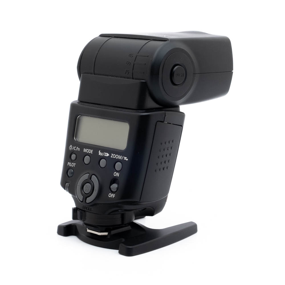 Canon Speedlite 430EX II - Käytetty, musta ulkoinen kamerasalama, jossa on nestekidenäyttö ja ohjauspainikkeet, on esillä pienellä muovijalustalla valkoista taustaa vasten.