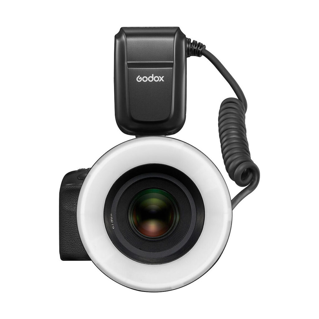 Godox_MF-R76_003 The black Godox MF-R76C TTL Macro Ring Flash - Canon is attached to the front of the camera lens, as seen from above. A circular flash surrounds the lens, and its power supply is connected by a twisted cable on top of it.