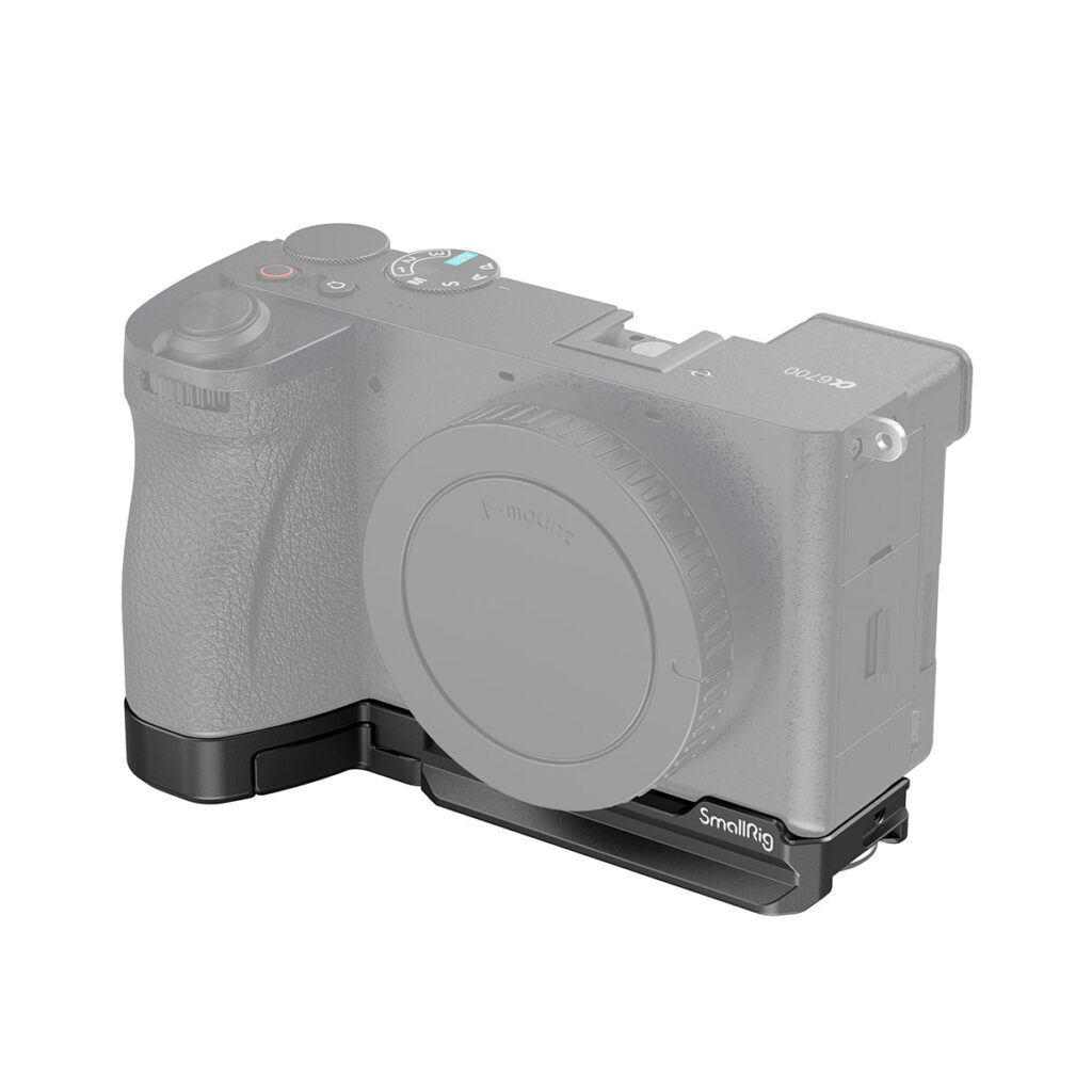 SmallRig_Baseplate_for_Sony_Alpha_6700_4338_001 Kamera, jossa on objektiivin kiinnityssuojus, on kuvassa kiinnitettynä SmallRig 4338 Baseplate for Sony Alpha 6700 -jalustaan, joka muodostaa L-kirjaimen muotoisen kiinnikkeen kameran vasemman alakulman ympärille. Kameran runko on osittain läpinäkyvä.