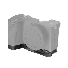 SmallRig_Baseplate_for_Sony_Alpha_6700_4338_001 Kamera, jossa on objektiivin kiinnityssuojus, on kuvassa kiinnitettynä SmallRig 4338 Baseplate for Sony Alpha 6700 -jalustaan, joka muodostaa L-kirjaimen muotoisen kiinnikkeen kameran vasemman alakulman ympärille. Kameran runko on osittain läpinäkyvä.