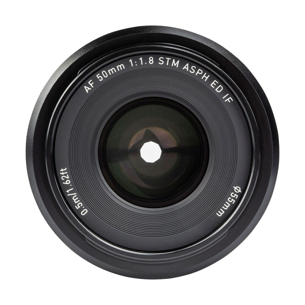 Viltrox_50mm_1.8_002 Lähikuvassa Viltrox AF 50mm f/1.8 -objektiivi, Sony E -objektiivin etuelementissä lukee "AF 50mm 1:1.8 STM ASPH ED IF, 0.5m/1.62ft ø55mm", ja siinä korostuvat aukko ja yksityiskohtaiset kaiverrukset.