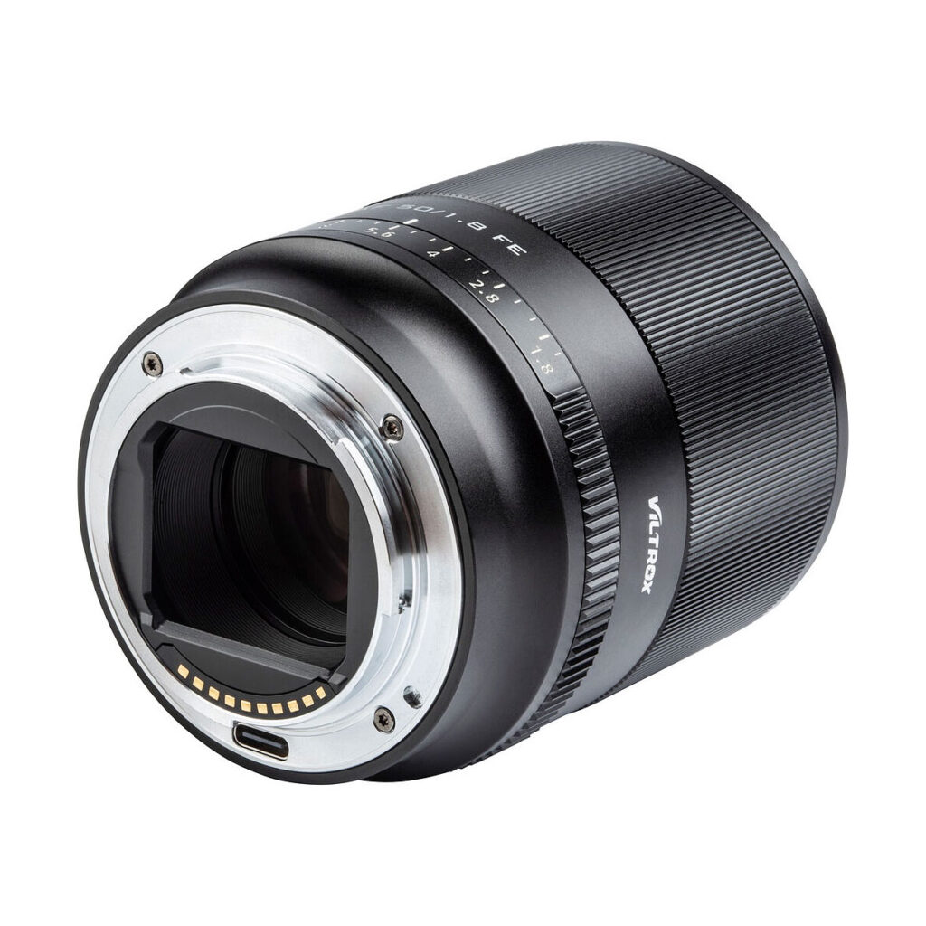 Viltrox_50mm_1.8_004 Lähikuvassa Viltrox AF 50mm f/1.8 -objektiivi Sony E:lle näkyy sen metallinen objektiivin kiinnitys, elektroniset kontaktit, aukon merkinnät ja kuvioitu tarkennusrengas valkoista taustaa vasten.