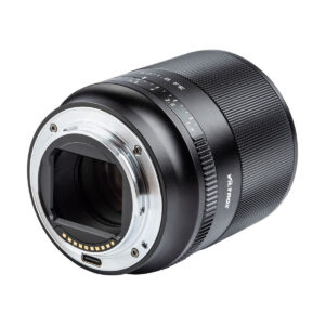 Viltrox_50mm_1.8_004 Lähikuvassa Viltrox AF 50mm f/1.8 -objektiivi Sony E:lle näkyy sen metallinen objektiivin kiinnitys, elektroniset kontaktit, aukon merkinnät ja kuvioitu tarkennusrengas valkoista taustaa vasten.
