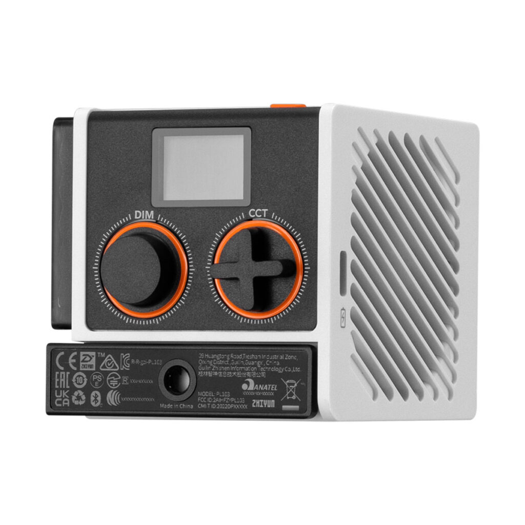 Zhiyun_Molus_g60_003 Zhiyun LED Molus G60 Combo COB -valaisin on kompakti elektroninen laite, jossa on pieni näyttö, kaksi suurta mustaa ja oranssia säätöpyörää, joissa on merkinnät DIM ja CCT, tuuletettu valkoinen sivupaneeli ja tarrat, joissa on sertifiointimerkinnät sen pohjassa.