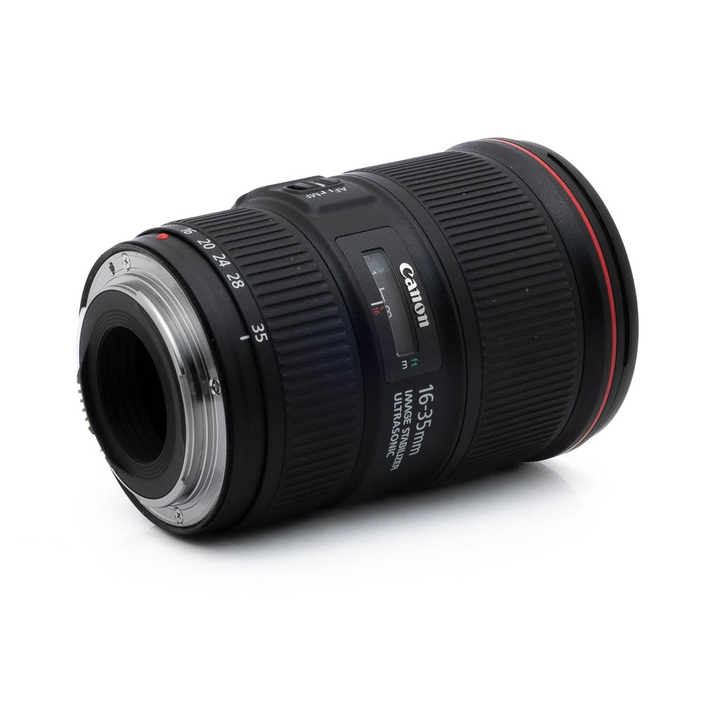Canon EF 16-35mm f/4 L IS USM - Käytetty laajakulmaobjektiivi makaa kyljellään, objektiivikiinnitys vasemmalla, ja sen musta runko, zoomausrengas ja erottuva punainen L-sarjan rengas etupuolen lähellä.