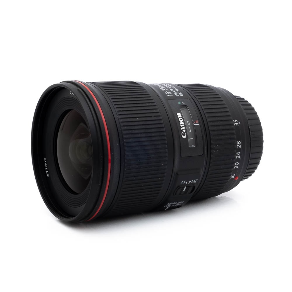 Canon EF 16-35mm f/4 L IS USM - Käytetty laajakulmaobjektiivi, jossa on punainen rengas, musta kuvioitu kahva ja zoomin/tarkennuksen kytkimet, on kuvassa kyljellään valkoista taustaa vasten.