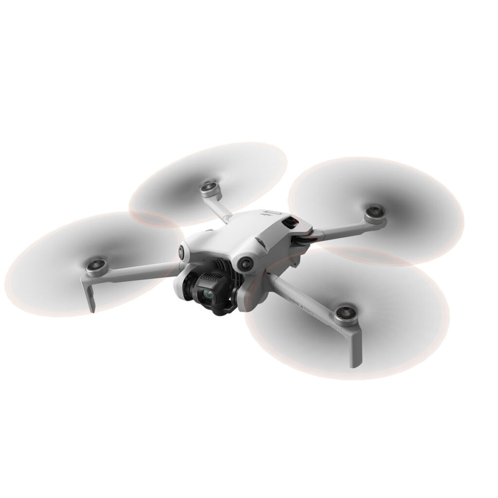 DJI_mini4pro_006 DJI Mini 4 Pro -lennokki, valkoinen nelikopteri, jossa on neljä potkuria ja asennettu kamera, näkyy kesken lennon valkoista taustaa vasten.