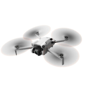 DJI_mini4pro_006 DJI Mini 4 Pro -lennokki, valkoinen nelikopteri, jossa on neljä potkuria ja asennettu kamera, näkyy kesken lennon valkoista taustaa vasten.