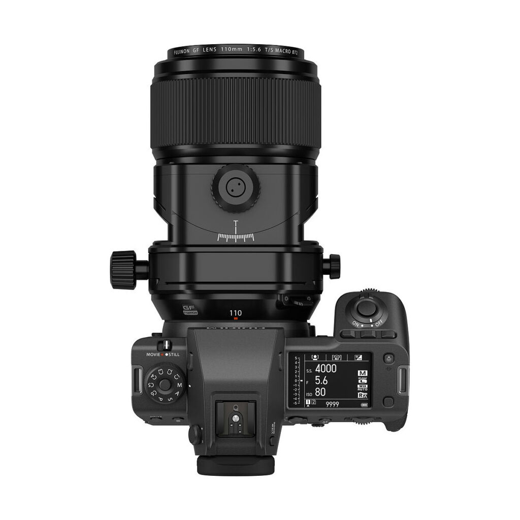 FujiFilm_Fujinon_110mm_GF_TS_005 Ylhäältä katsottuna Fujifilm Fujinon GF 110mm f/5.6 T/S -objektiivi kiinnitettynä digitaalikameraan, jossa näyttö ja säätimet näyttävät ISO-, aukko- ja suljinaika-asetukset tavallista valkoista taustaa vasten.