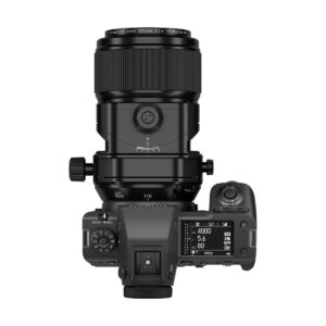FujiFilm_Fujinon_110mm_GF_TS_005 Ylhäältä katsottuna Fujifilm Fujinon GF 110mm f/5.6 T/S -objektiivi kiinnitettynä digitaalikameraan, jossa näyttö ja säätimet näyttävät ISO-, aukko- ja suljinaika-asetukset tavallista valkoista taustaa vasten.