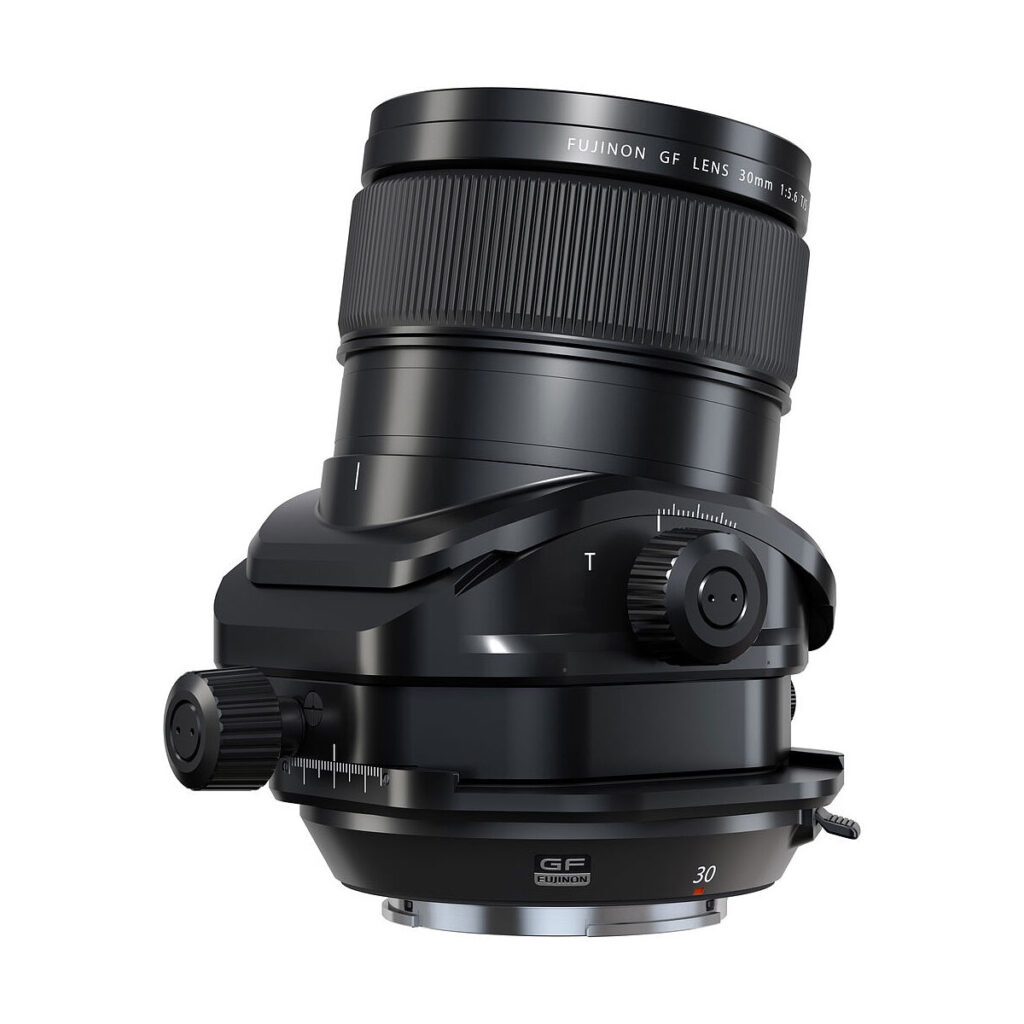 FujiFilm_Fujinon_30mm_GF_TS_002 Fujifilm Fujinon GF 30mm f/5.6 T/S -objektiivi mustana, jossa on säätönupit ja tilt-shift-mekanismi, kuvattuna kulmassa valkoisella taustalla.