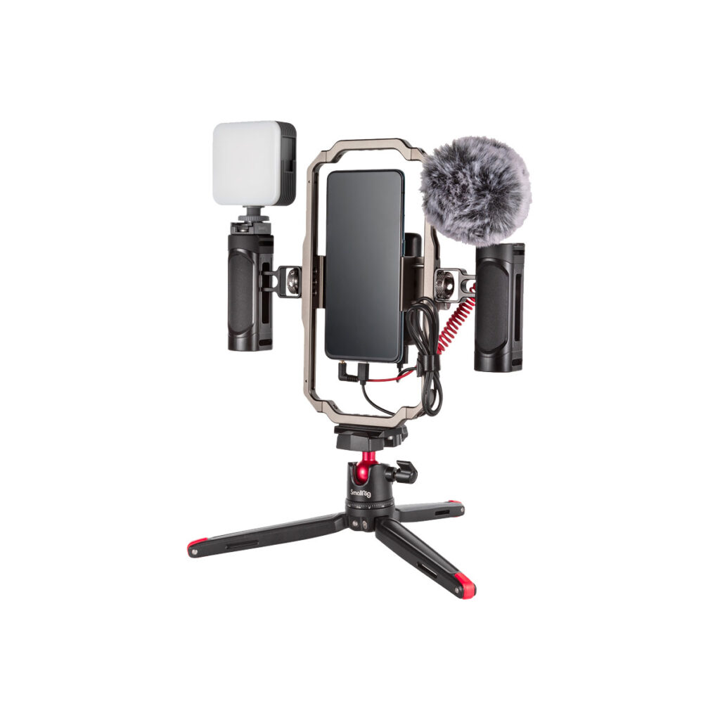 Smallrig_3384_001 SmallRig 3384 Professional Vlogging Kit sisältää älypuhelimen, joka on kiinnitetty suorakulmaisella kehyksellä varustettuun jalustaan, LED-valon vasemmalla puolella ja ulkoisen mikrofonin, jossa on karvainen tuulisuoja oikealla puolella.
