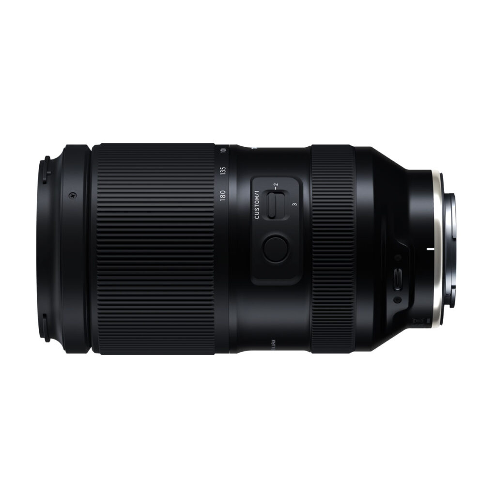 Tamron_70-180_GN_004 Tamron 70-180mm F/2.8 Di III VC VXD G2 -objektiivi Sony E:lle on esitetty sivuprofiilissa, jossa on mustat kuvioidut zoom- ja tarkennusrenkaat, säätökytkimet ja metallinen kiinnike valkoista taustaa vasten.