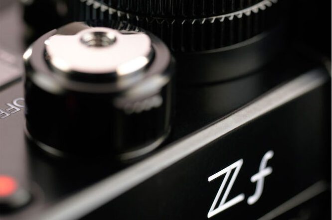 nikon_zf_02 Lähikuva Nikon Zf -järjestelmäkamerasta, musta, keskittyen "Zf"-logoon ja metalliseen säätöpyörään, jossa on yksityiskohtaisia kuvioita.