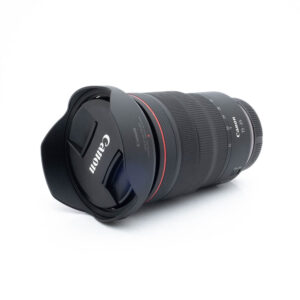 Canon RF 15-35mm f/2.8 L IS USM (Takuuta 6kk) - Käytetty objektiivi vastavalosuojalla lepää valkoisella pinnalla, ja sen musta runko, punainen rengas ja näkyvä Canon-brändi objektiivin suojuksessa ovat esillä.