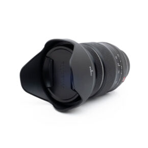 Fujinon 16-55mm f28 R LM WR-3 Fujinon GF 50mm f/3.5 R LM WR (sis.ALV24%) - Käytetty musta kameraobjektiivi, johon on kiinnitetty vastavalosuoja ja suojus, näkyy valkoisella taustalla, ja siinä näkyy objektiivin etupuoli ja osa objektiivin piipusta.