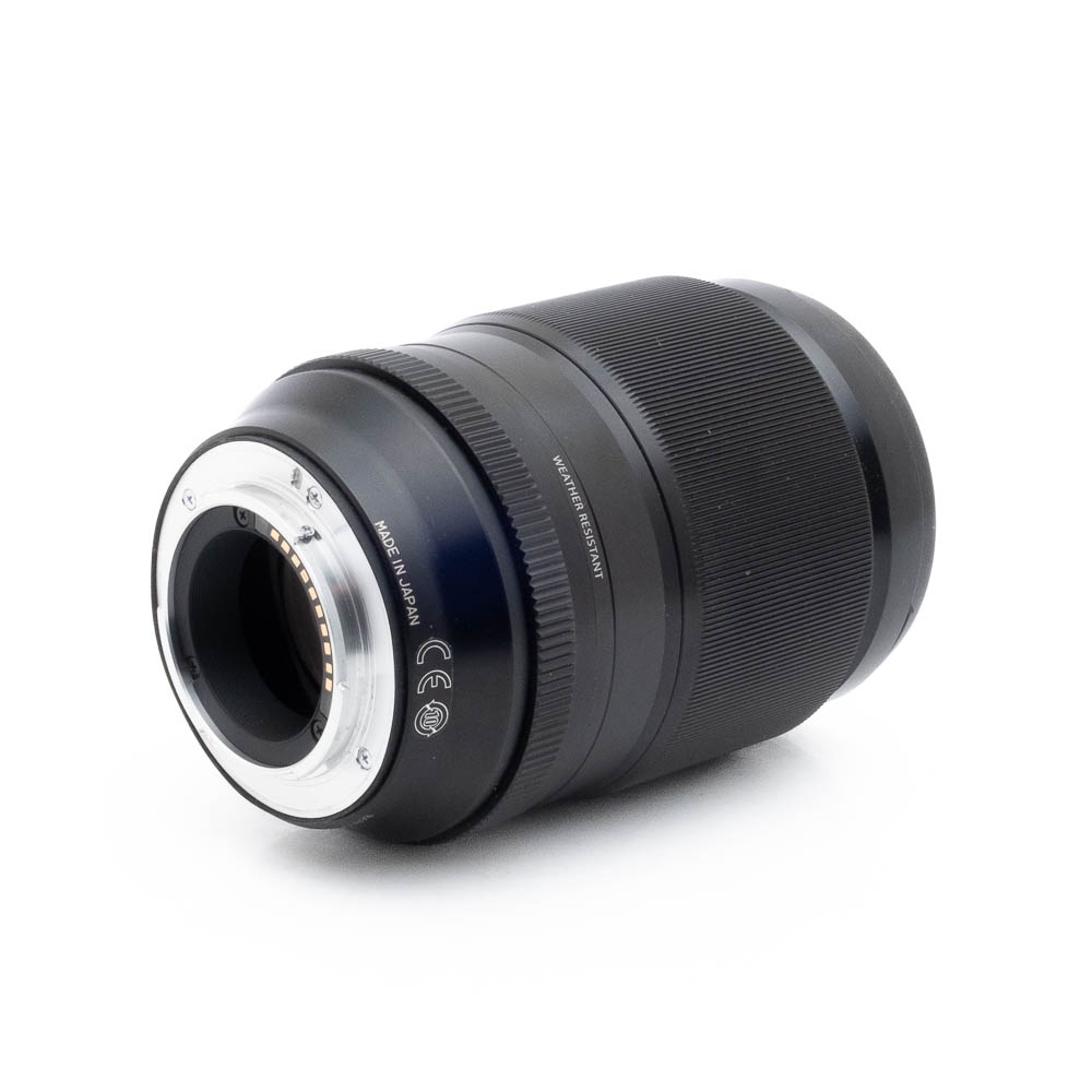 Fujinon 90mm f2 R LM WR-1-2 Fujinon GF 50mm f/3.5 R LM WR (sis.ALV24%) - Käytetty musta kameraobjektiivi on näytetty kyljellään valkoista taustaa vasten, ja siinä näkyy metallinen objektiivin kiinnitys ja elektroniset kontaktit.