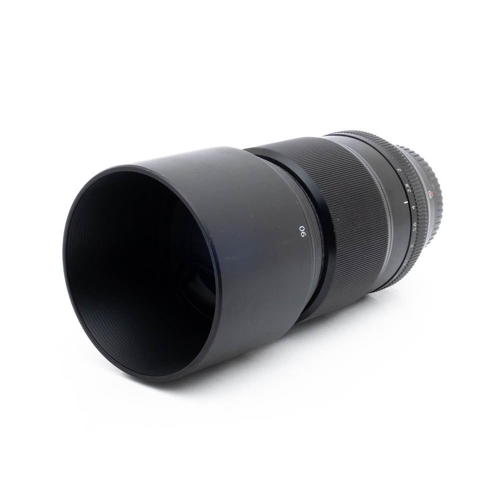 Fujinon 90mm f2 R LM WR-3-2 Fujinon GF 50mm f/3.5 R LM WR (sis.ALV24%) - Käytetty kameran objektiivi, johon on kiinnitetty pitkä lieriömäinen huppu, lepää kyljellään valkoista taustaa vasten.