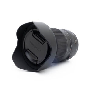 Fujinon GF 23mm f4 R LM WR-3 Fujinon GF 50mm f/3.5 R LM WR (sis.ALV24%) - Käytetty kameran objektiivi, johon on kiinnitetty vastavalosuoja ja suojus, makaa kyljellään valkoista taustaa vasten.