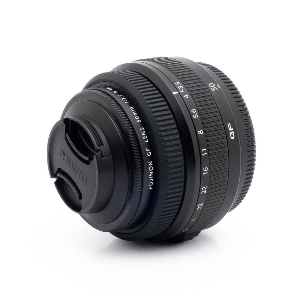 Fujinon GF 50mm f35 R LM WR-3 Fujinon GF 50mm f/3.5 R LM WR (sis.ALV24%) - Käytetty -objektiivi näkyy valkoisella taustalla, kun objektiivin suojus on kiinnitetty ja tarkennusrengas ja aukkorenkaat ovat näkyvissä.
