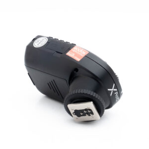 Godox Xpro C-1 Käytetty Godox XPro Canonin langaton mustan värinen salamalaukaisin, jossa on painikkeet, näyttö ja näkyvä hot shoe -kiinnitys, kuvattuna kulmassa valkoisella taustalla.