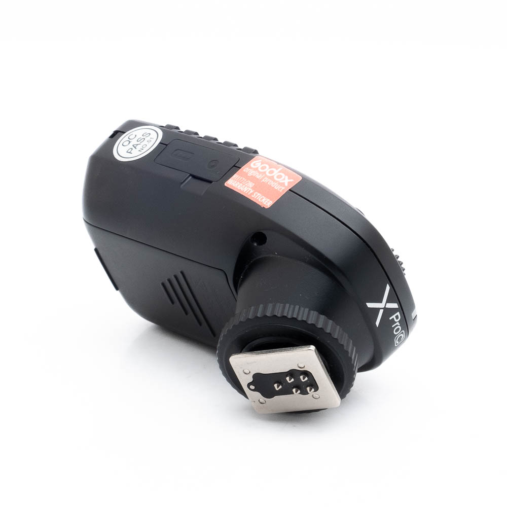 Godox Xpro C-1 Käytetty Godox XPro Canonin langaton mustan värinen salamalaukaisin, jossa on painikkeet, näyttö ja näkyvä hot shoe -kiinnitys, kuvattuna kulmassa valkoisella taustalla.