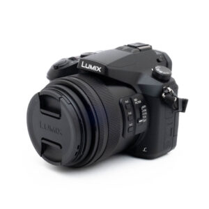 Lumix FZ-2000-4 Fujinon GF 50mm f/3.5 R LM WR (sis.ALV24%) - Käytetty -objektiivi on kuvassa suojus päällä, hieman vasemmalle kallistettuna valkoisella taustalla. Objektiivin rungossa näkyy erilaisia säätimiä ja painikkeita.