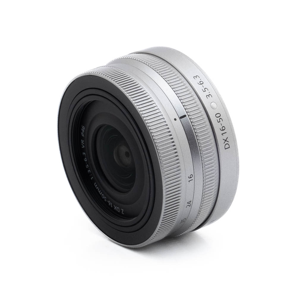 Nikon Z DX 16-50mm f35-63-2-2 Hopeinen Fujinon GF 50mm f/3.5 R LM WR (sis.ALV24%) - Käytetty objektiivi, jossa on kuvioitu tarkennusrengas ja kaiverretut merkinnät, vinossa valkoisella pohjalla.