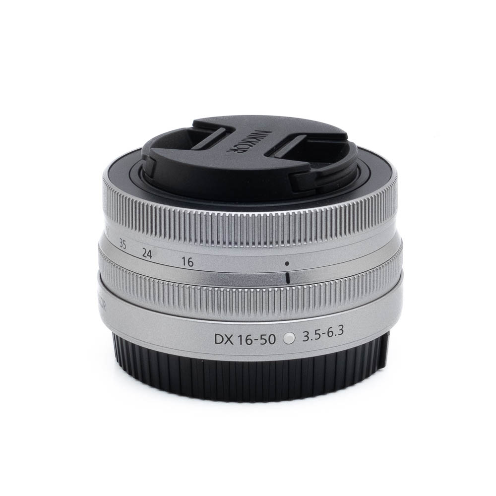 Nikon Z DX 16-50mm f35-63-3-2 Fujinon GF 50mm f/3.5 R LM WR (sis.ALV24%) - Käytetty kameran objektiivi, johon on kiinnitetty musta objektiivin suojus, valkoista taustaa vasten.