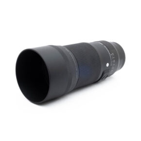 Fujinon GF 50mm f/3.5 R LM WR (sis.ALV24%) - Käytetty musta teleobjektiivi, jossa on suuri linssinsuojus, makaa vinossa valkoisella pinnalla.