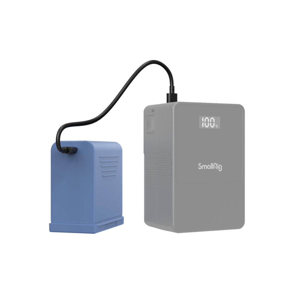 SmallRig_2467_005 Sininen akku on liitetty mustalla kaapelilla harmaaseen SmallRig 4267 USB-C ladattavaan kamera-akkuun NP-F970, jonka digitaalinäyttö näyttää 100 % valkoisella pohjalla.