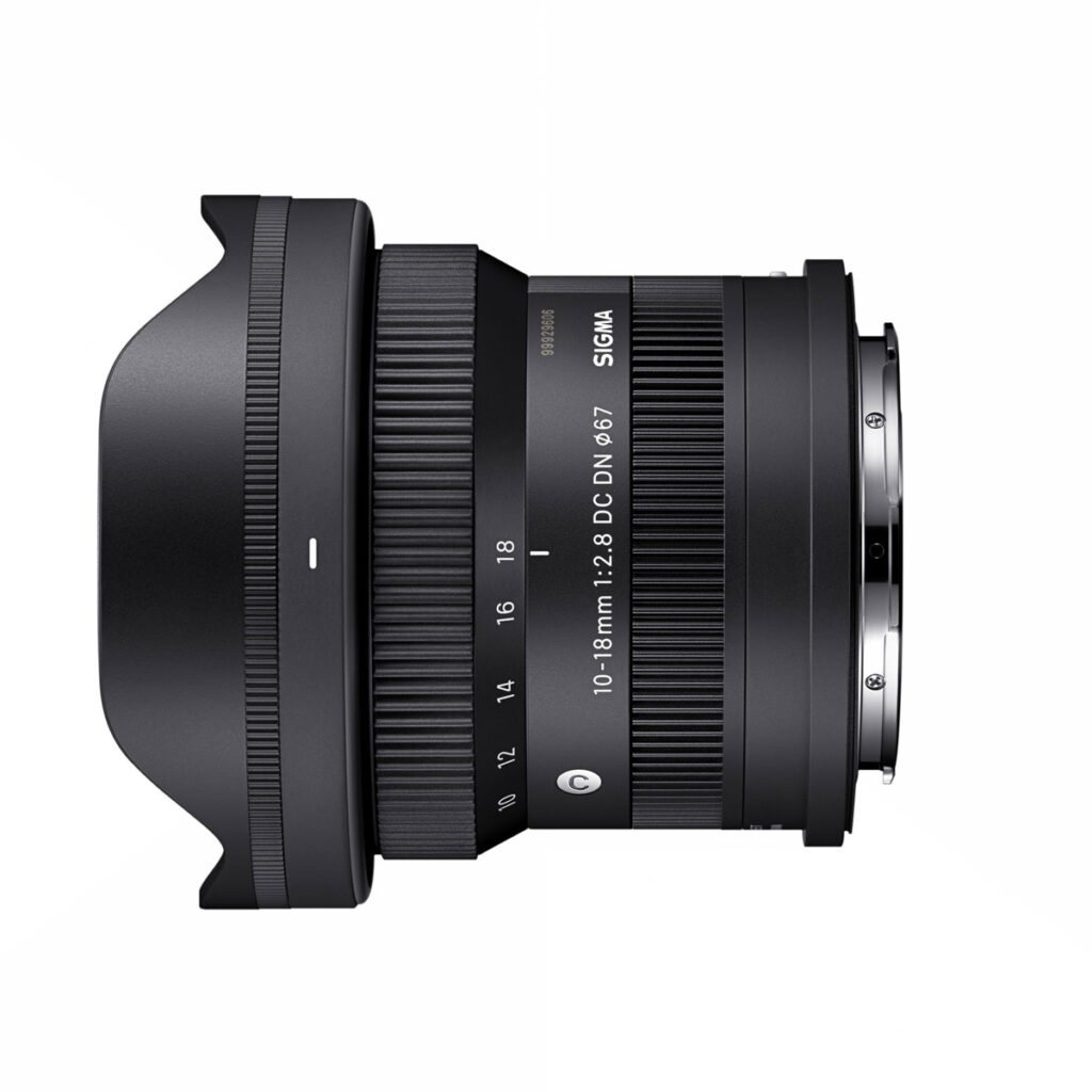 sigma_10-18mm_f28_03 Sigma 10-18mm f/2.8 DC DN -objektiivi, Sony E, sivuprofiili näkyy valkoisella taustalla, jossa näkyy sen musta viimeistely, zoomaus- ja tarkennusrenkaat, vastavalosuoja ja kiinnitys.