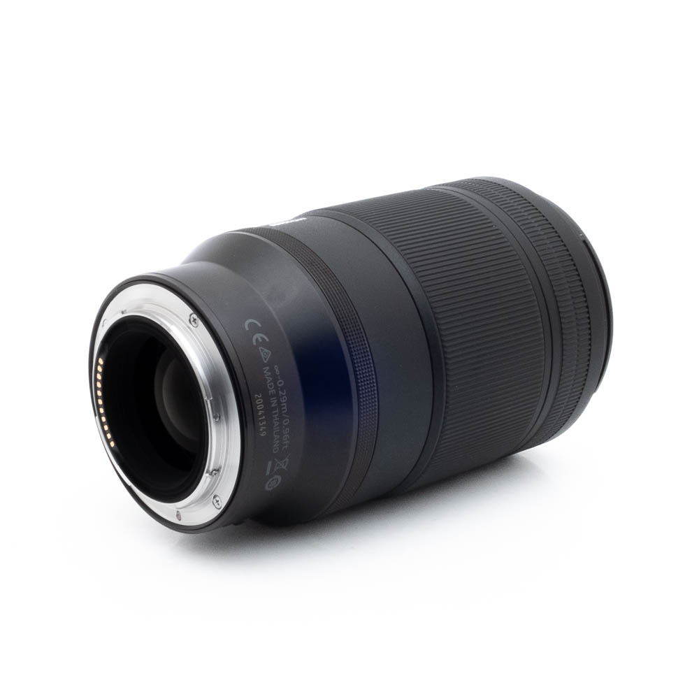 Nikon Z MC 105mm f28 S-1 Nikon Nikkor Z MC 105mm f/2.8 VR S (Kunto K5) - Käytetty musta kameraobjektiivi makaa kyljellään, ja siinä näkyy metallinen objektiivin kiinnitys ja elektroniset kontaktit toisessa päässä valkoista taustaa vasten.
