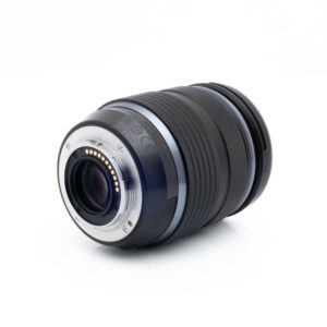 Olympus 12-40mm f28 PRO-1-3 Lähikuva Nikon Nikkor Z MC 105mm f/2.8 VR S (Kunto K5) - Käytetty -objektiivista, joka on kuvattu kyljellään, elektroniset koskettimet ja kiinnitys näkyvissä, kuvioitu musta tynnyri, jossa on hopeisia ja sinisiä korostuksia valkoista taustaa vasten.