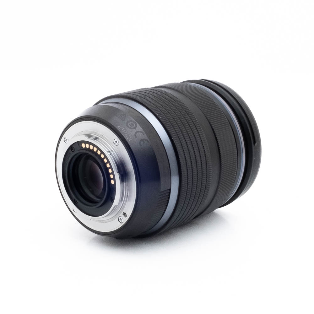 Olympus 12-40mm f28 PRO-1-3 Lähikuva Nikon Nikkor Z MC 105mm f/2.8 VR S (Kunto K5) - Käytetty -objektiivista, joka on kuvattu kyljellään, elektroniset koskettimet ja kiinnitys näkyvissä, kuvioitu musta tynnyri, jossa on hopeisia ja sinisiä korostuksia valkoista taustaa vasten.