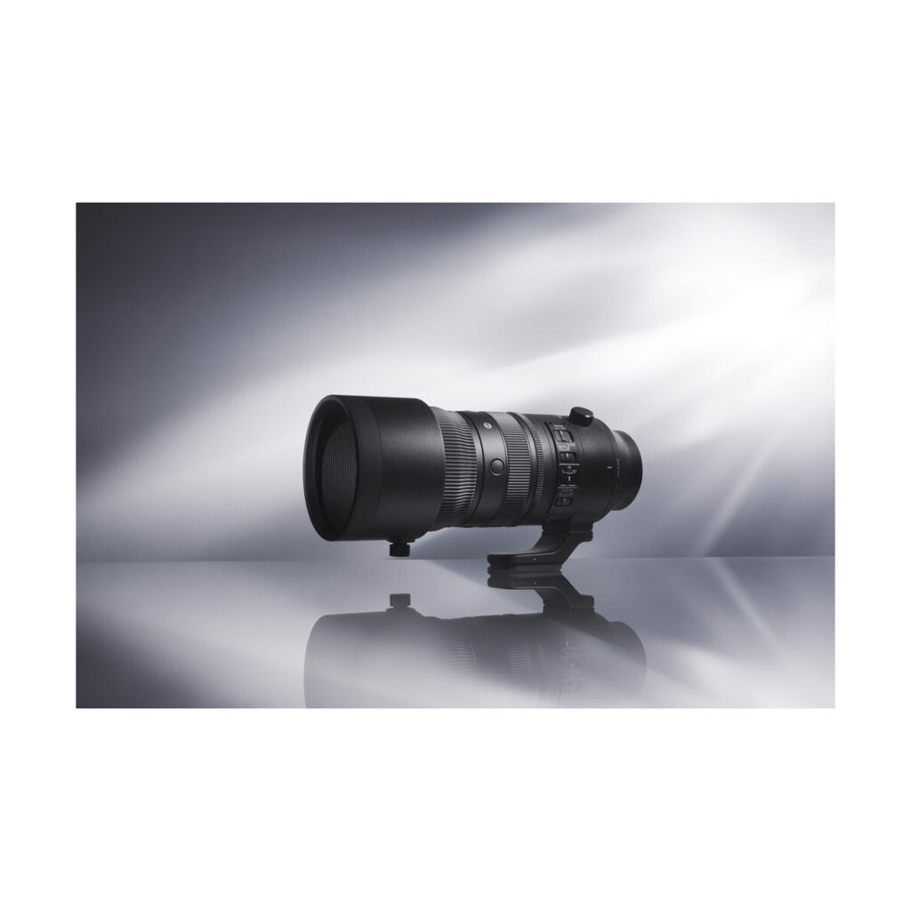 sigma_70-200_sport_dn_02 Sigma 70-200mm f/2.8 DG DN OS Sport -objektiivi Sony E:lle, jossa on jalustakiinnitys, näkyy heijastavalla pinnalla pehmeästi valaistua, harmaata taustaa vasten.