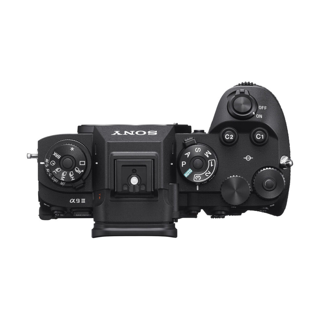 sony_a9_iii_02 Mustan Sony A9 III -järjestelmäkameran ylhäältä alaspäin näkymä, jossa näkyvät säätöpyörät, painikkeet ja kytkimet, kuten moodivalitsin, on/off-kytkin, suljinpainike ja mukautetut toimintopainikkeet.