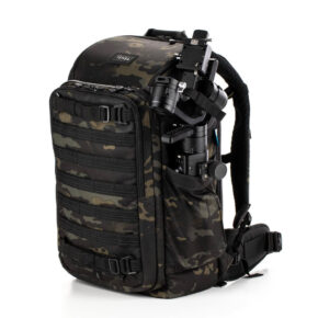 Tenba Axis v2 24L reppu MultiCammusta -kamerareppu, jossa on musta naamiointi, useita vetoketjulokeroita ja MOLLE-verkko, pitää sisällään sivulleen kiinnitetyn kameragimbalin.