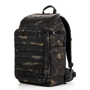 Tenba Axis v2 32L Backpack MultiCam -kamerareppu sisältää mustan ja tummanvihreän maastokuvion, useita vetoketjulokeroita, säädettävät hihnat ja yläkahvan, kuvassa valkoisella pohjalla.