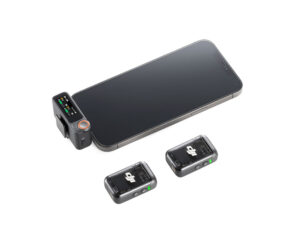 DJI_Mic2_1+2_004 Älypuhelin kytketty DJI Mic 2 Dual Kit -langaton mikrofonijärjestelmä vastaanotin, jossa on kaksi kompakti musta langaton lähetin sijoitettu lähelle valkoiselle pinnalle.