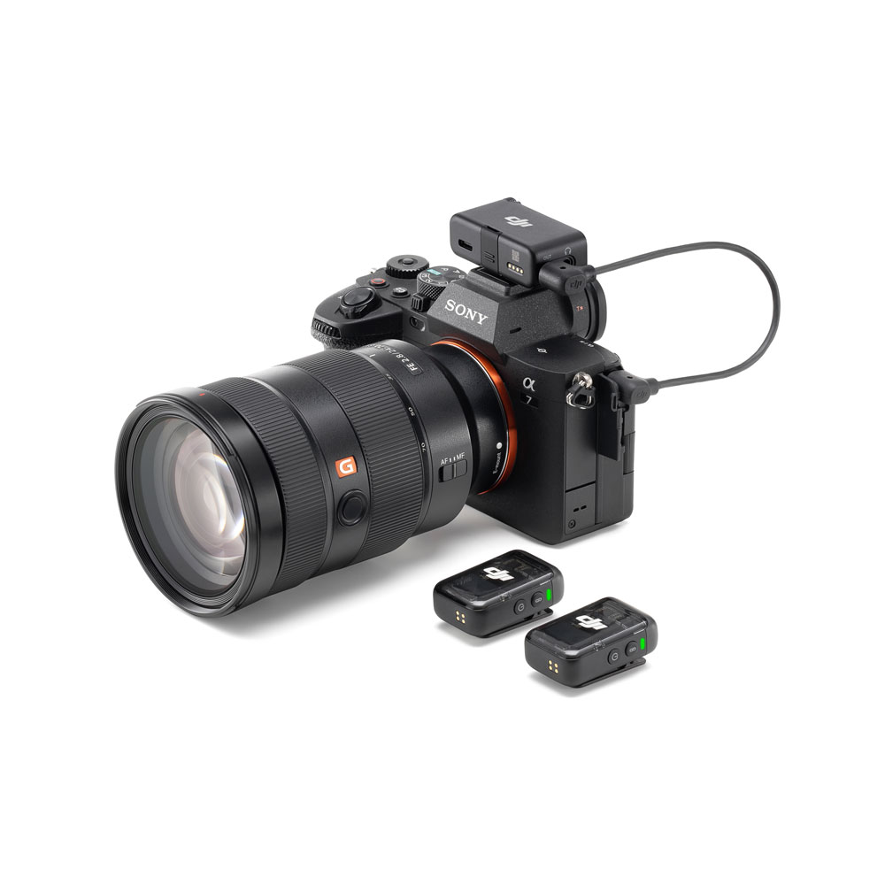 DJI_Mic2_1+2_006 Sony Alpha -kamera, jossa on suuri G Master -objektiivi, DJI Mic 2 Dual Kit -langaton mikrofonivastaanotin asennettuna kameran päälle ja kaksi langatonta lähetintä samasta sarjasta kameran edessä.