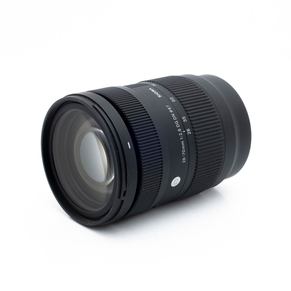 Sigma 28-70mm f/2.8 DG DN C L-Mount - Käytetty on kuvattu kulmassa valkoisella taustalla, ja kuvassa näkyvät musta runko, tarkennusrengas, zoomausrengas, polttovälimerkinnät (28-70mm) ja tuotemerkin merkintä.
