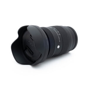 Musta Sigma 28-70mm f/2.8 DG DN C L-Mount - Käytetty -objektiivi, johon on kiinnitetty vastavalosuoja, kuvattuna kulmassa valkoisella taustalla ja jossa näkyy erilaisia asetuksia ja merkintöjä objektiivin rungossa.