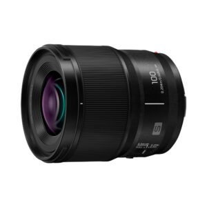 panasonic_100mm_macro_01 Panasonic Lumix S 100mm F/2.8 macro -objektiivi on musta objektiivi, jonka sivulle on painettu "100" ja "0.20m/0.66ft", kuvioitu tarkennusrengas ja heijastava lasielementti valkoista taustaa vasten.