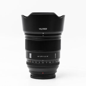 viltrox_27mm_pro_01 Musta Viltrox AF PRO 27mm f/1.2 -objektiivi, Fuji X seisoo pystyasennossa valkoisella pohjalla, jossa on terälehdellä muotoiltu huppu, tarkennusrengas ja aukkorenkaat, joissa on merkityt numerot.