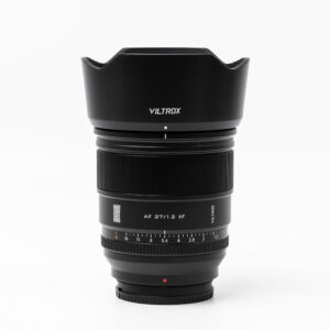 Musta Viltrox AF PRO 27mm f/1.2 -objektiivi, Fuji X seisoo pystyasennossa valkoisella pohjalla, jossa on terälehdellä muotoiltu huppu, tarkennusrengas ja aukkorenkaat, joissa on merkityt numerot.