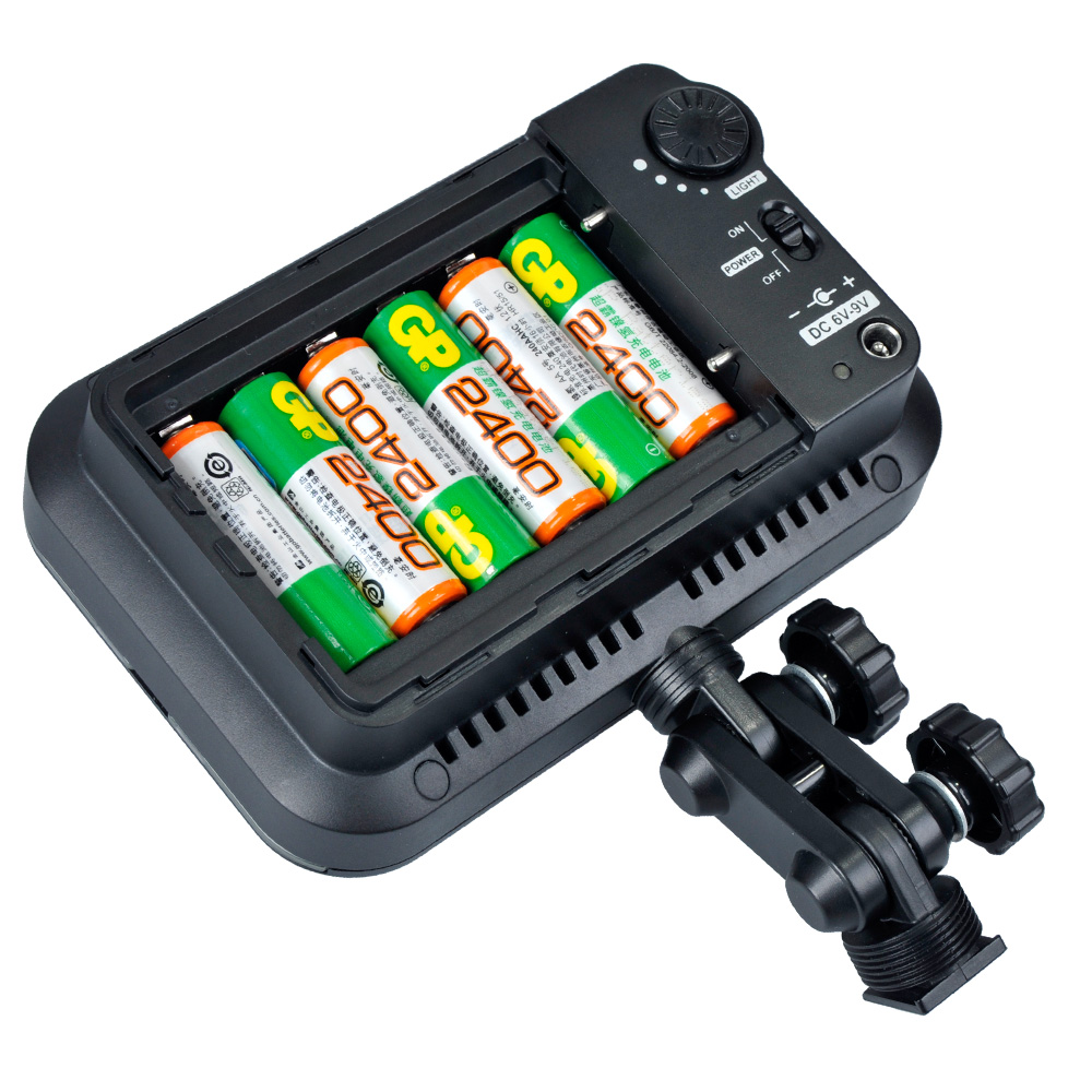 1373351142_696 Godox Led 126 musta LED-videovalaisin, jonka paristolokero on avattu ja jonka sisältä paljastuu neljä AA-paristoa. Valon vieressä on kiinnitysteline, jossa on säädettävät nupit.