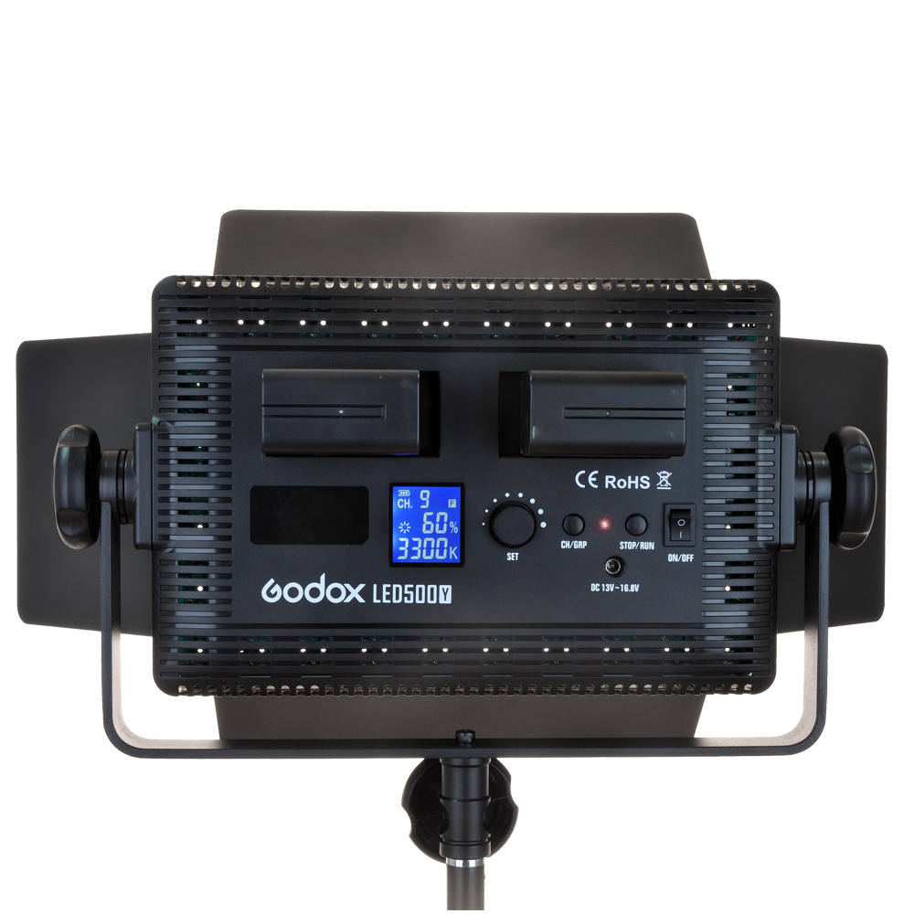 Godox LED 500C Bi-Color -valaisimen takanäkymä, jossa näkyy kaksi akkupaikkaa, säädettävät lato-ovet, ohjauspaneeli ja LCD-näyttö, joka näyttää asetukset, asennettuna valaisinjalustaan.