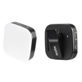 1520547883_648 Two compact, square-shaped Godox LED M32 luminaires are on display; one has a smooth white front panel, while the other has a black rear panel with a clip and charging port.