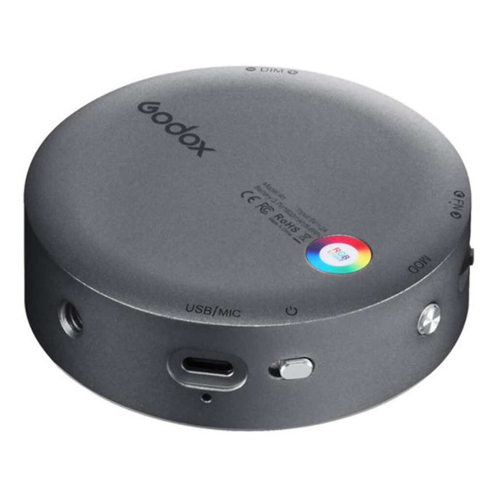 1600865322_591 Godox R1 Mobile RGB LED-valaisin - Harmaa on pyöreä, harmaa laite, jossa on USB/MIC-portti, painikkeet, merkkivalot ja pieni monivärinen pyöreä kosketusnäyttö, jonka päällä on Godox-merkin nimi.